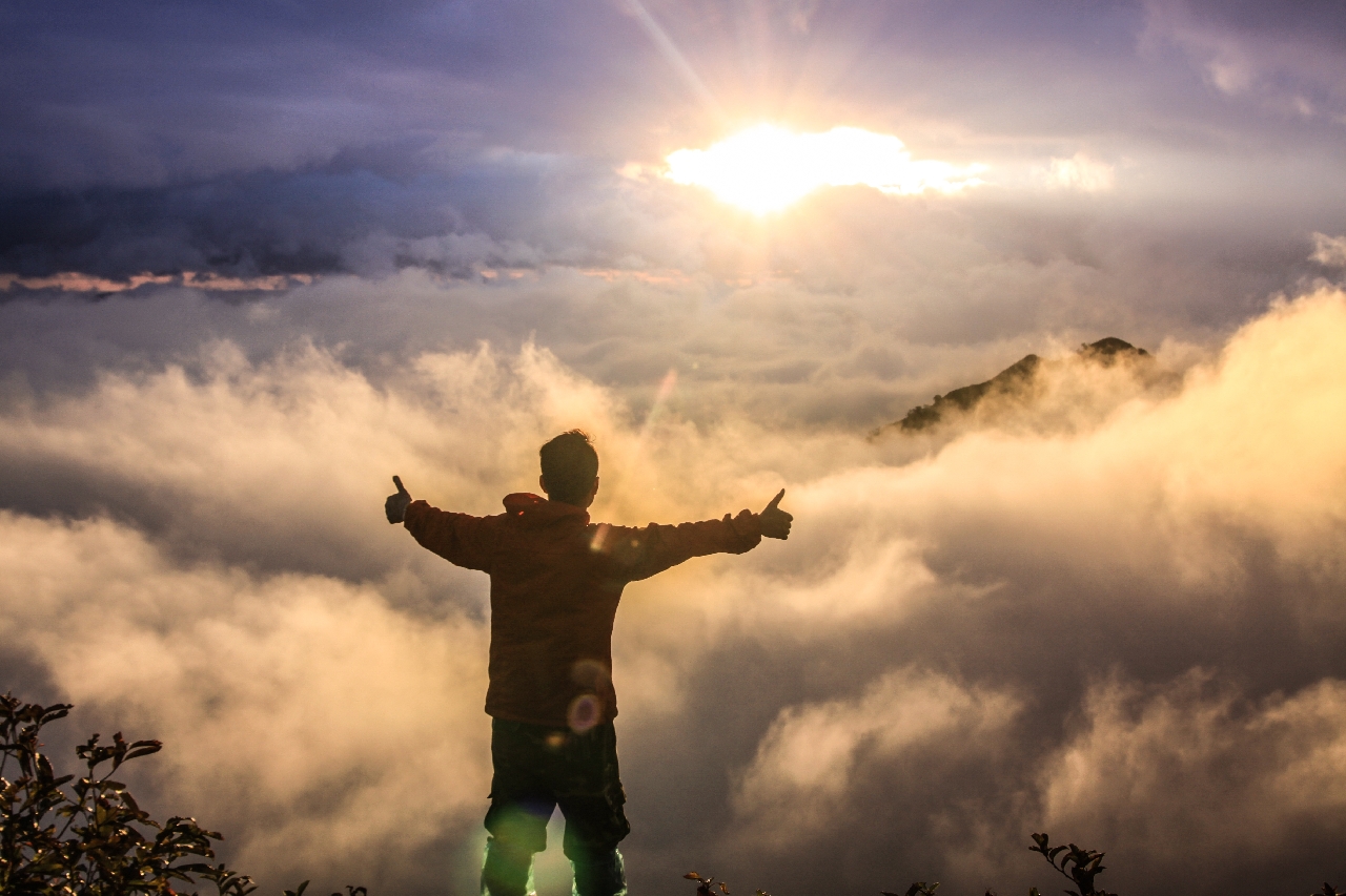 Man standing above the clouds with arms outstretched at sunrise