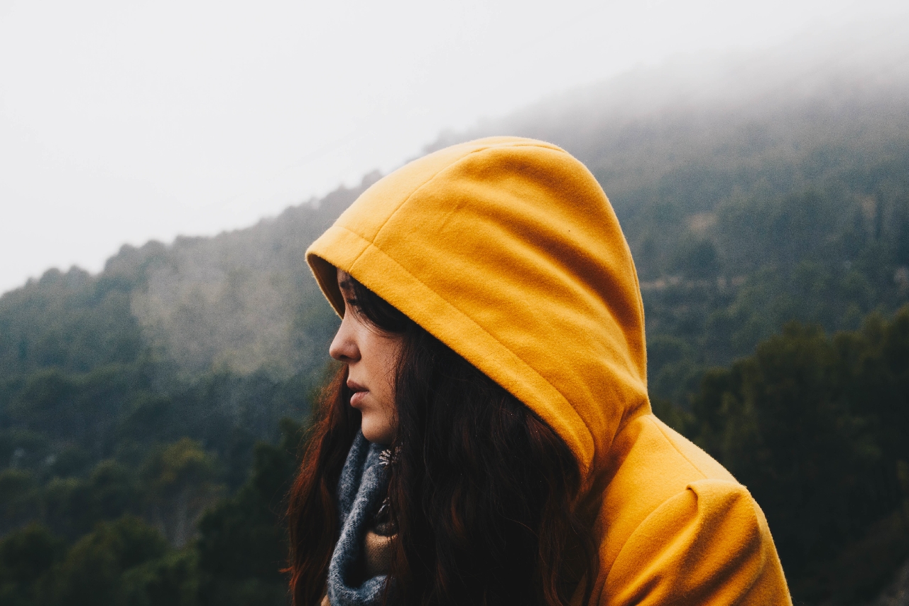 A side profile of a woman in a yellow hoodie in the mountains