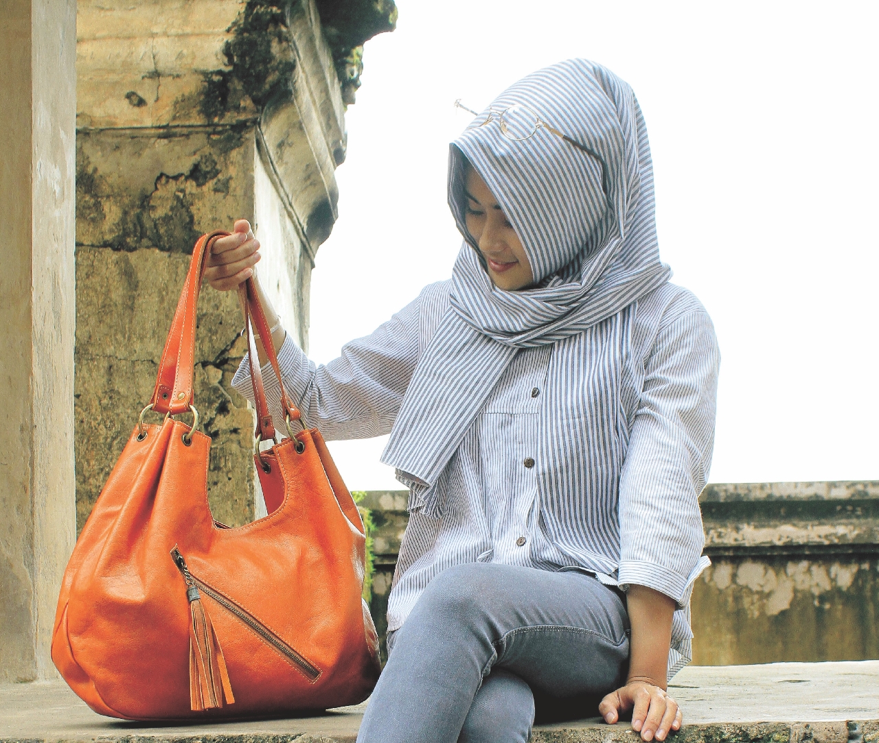 A woman holding a large orange handbag while sitting on a step