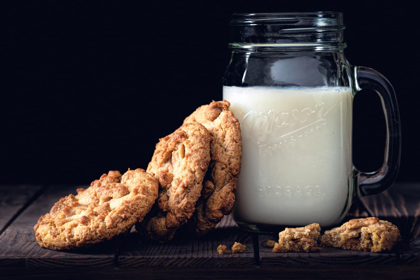 Three cookies leaning against a jar of milk