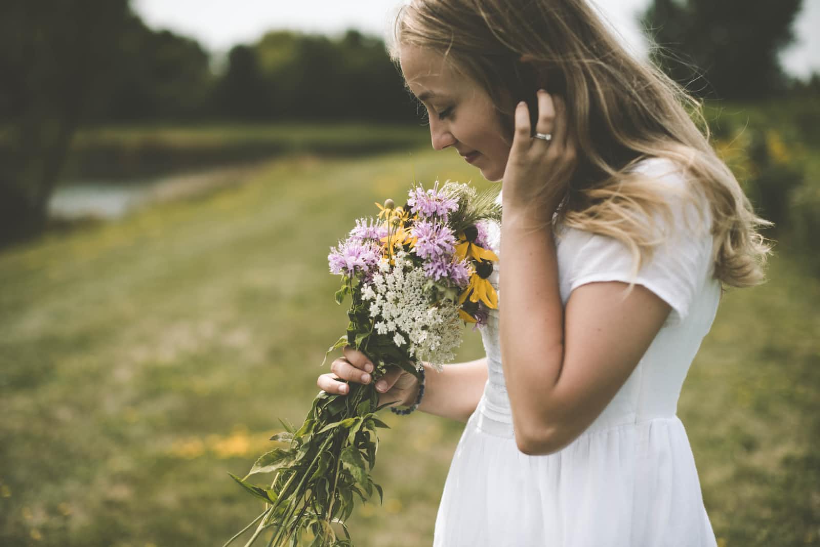 A woman in a white dress smelling flowers in an open field